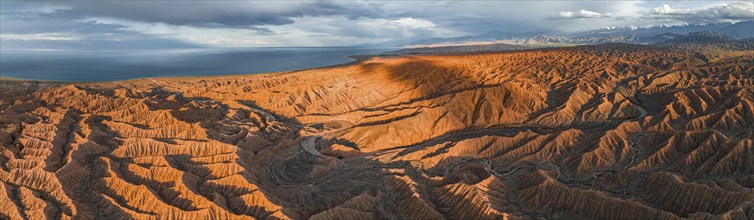 Panorama, landscape of eroded hills, badlands at sunset, behind Issyk Kul Lake and mountain peaks