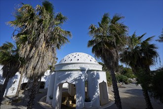 White building with domed roof and palm trees, shown under a clear blue sky, thermal springs,