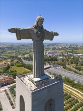 Large statue of Jesus with outstretched arms on a platform, overlooking the cityscape on a clear