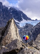 Woman with colorful open umbrella between large rocks, glacier Lenangsbreen, at glacier lake