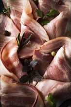 Raw bacon, sliced, with micro greenery and spices, on a black background, close-up