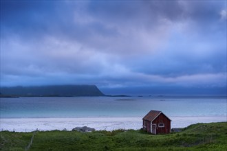 A red wooden hut on the sandy beach of Ramberg (Rambergstranda), sea and mountains. At night at the