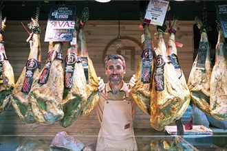 Castilian man, 40 years old, between Iberico hams for sale at the Mercado Central, Salamanca,