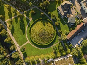 Aerial view of a green Celtic burial mound with circular path surrounded by houses and trees,