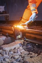 Worker working on rails with sparks, wearing orange work outfit, welding rails, track construction