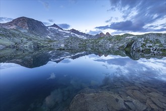 Calm lake reflects the surrounding mountains and the cloudy sky at sunrise, Krimml, Salzburg,