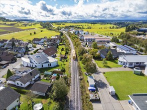 View over a village with railway line, surrounded by green fields and a clear sky, tamping machine,