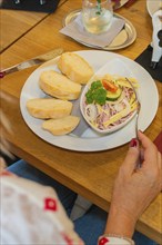 Sausage salad with onions, gherkins and tomatoes, served with bread. One hand holding a fork,