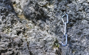 A carabiner hangs from a hook on a rock face. Climbers use the so-called quickdraws to secure