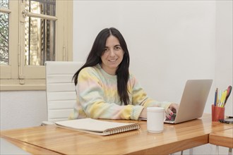 Portrait of a smiling young woman working on laptop computer at home