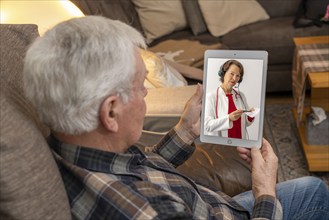 Symbolic image of telemedicine, elderly patient speaking to a doctor in a video conference from