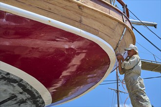 A worker is working on the red hull of a sailing ship, Patmos Marine, boatyard, Diakofti, Patmos,