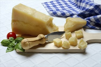 A piece of Parmesan cheese and chopped pieces of cheese on a wooden board