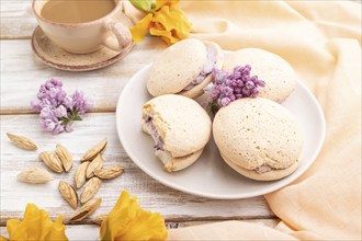 Meringues cakes with cup of coffee on a white wooden background and orange linen textile. Side