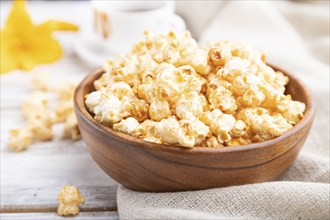 Popcorn with caramel in wooden bowl and a cup of coffee on a white wooden background and linen