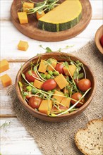 Vegetarian vegetable salad of tomatoes, pumpkin, microgreen pea sprouts on white wooden background