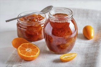 Tangerine and kumquat jam in a glass jar with fresh fruits on white background. Homemade, close up