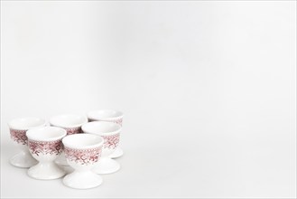 A set of white and red ceramic egg cups with a floral pattern arranged on a light-coloured