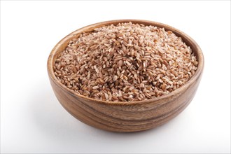 Wooden bowl with unpolished brown rice isolated on white background. Side view, close up