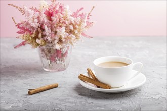 Pink and red astilbe flowers in glass and a cup of coffee on a gray and pink background. Morninig,