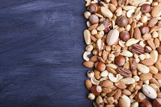 Mixed different kinds of nuts on black wooden background. hazelnut, brazil nut, almond, pumpkin