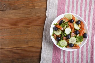 Vegetarian salad of tomatoes, cucumbers, parsley, olives and mustard on linen tablecloth, top view,