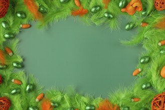 Lively Easter background in green and orange with feathers, eggs and carrots forming a frame