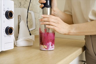 Hands of a woman mixing fruits and berries in a blender for smoothie