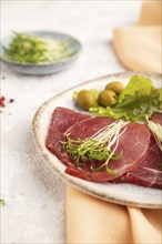 Slices of smoked salted meat with cilantro microgreen on gray concrete background and orange