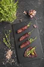 Slices of smoked salted meat with green pea microgreen on black concrete background. Top view, flat