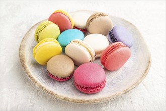 Multicolored macaroons on ceramic plate on gray concrete background. side view, still life, close