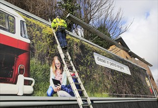 Man standing on ladder billboard for 'diesel in petrol engine' placed on advertising sign, city of