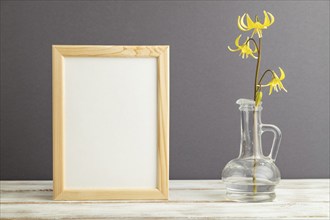 Wooden frame with yellow trout lily or dogtooth violet flowers in glass on gray pastel background.