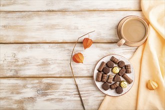 Chocolate candies with cup of coffee and physalis flowers on a white wooden background and orange