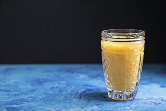 Glass of orange juice on a black and blue background. Hard light, contrast. Side view, copy space