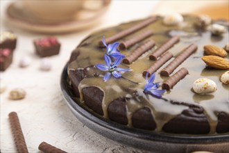 Homemade chocolate brownie cake with caramel cream and almonds with cup of coffee on a white