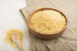 Wooden bowl with raw golden rice and wooden spoon on a white wooden background and linen textile.