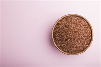 Wooden bowl with raw red quinoa seeds on a pastel pink background. Top view, flat lay, copy space