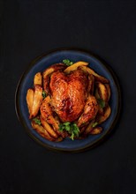 Fried whole chicken, with potatoes, on a black background, no people