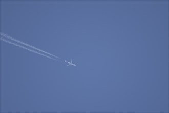 Jet aircraft in flight with a contrail or vapour trail across a blue sky, England, United Kingdom,