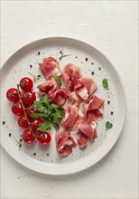 Sliced prosciutto, appetizer, with cherry tomatoes, on a white plate, top view