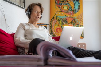 Woman, mid-50s, works from home, with laptop and communicates with colleagues via headset, home