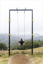 Young woman sits on a swing, Cerro Pico de Novio, Chiloe, Chile, South America