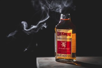 A single whisky bottle with smoke against a dark background