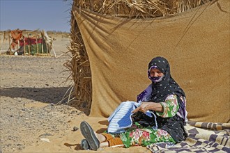 Elderly nomadic Bedouin woman with hijab unravelling woollen garment in the Sahara Desert near