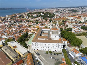 Aerial view of a coastal town with red roofs, white buildings, a bridge and green trees, aerial