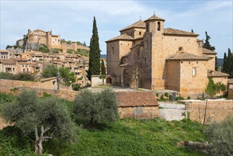 A historic town with medieval buildings and a stone church surrounded by cypresses and trees under