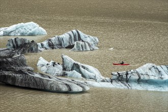 Single kayaker in red kayak, glacial lake at the glacier solheimajökull, icebergs on the lake,