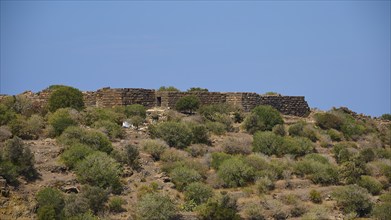 Ancient ruined wall in an arid landscape under a blue sky with low vegetation, Palaiokastro,