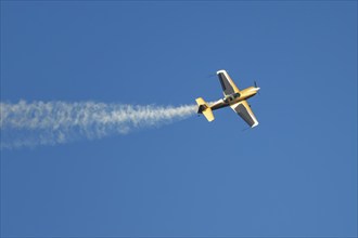 Golden stunt aerobatic plane performing stunts in blue sky with smoke trail. Concept of speed,